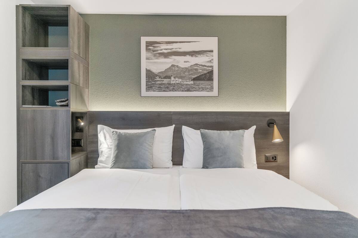 Une chambre moderne avec un grand lit, une tête de lit dotée d’étagères intégrées, un tableau encadré au mur et une lampe de chevet.