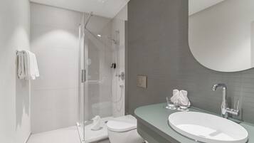 Un baño moderno con cabina de ducha de vidrio, inodoro blanco y un lavamanos ovalado grande con espejo sobre él.