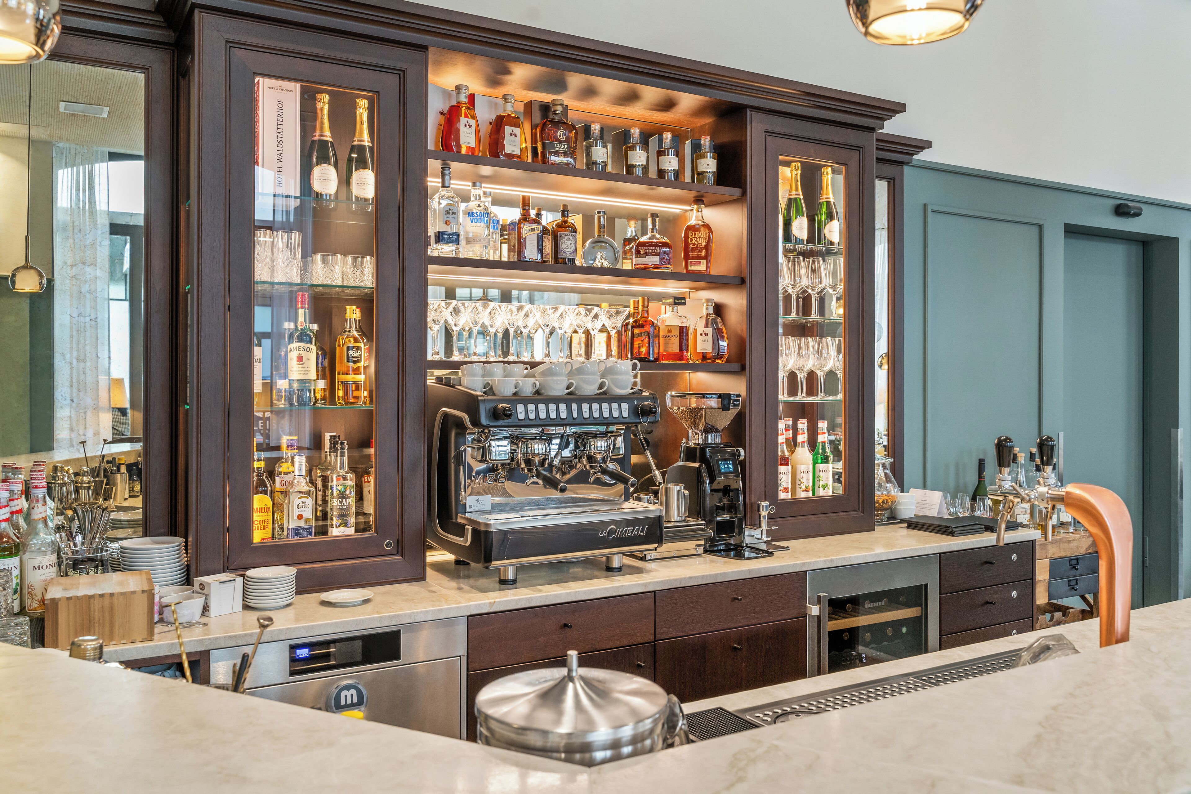 A bar area with a coffee machine, shelves of liquor bottles, and glasses.