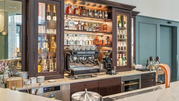 A bar area with a coffee machine, shelves of liquor bottles, and glasses.