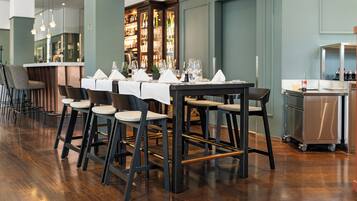 Un restaurante con una larga mesa dispuesta para comer, taburetes de bar y una zona de bar con estantes llenos de botellas.