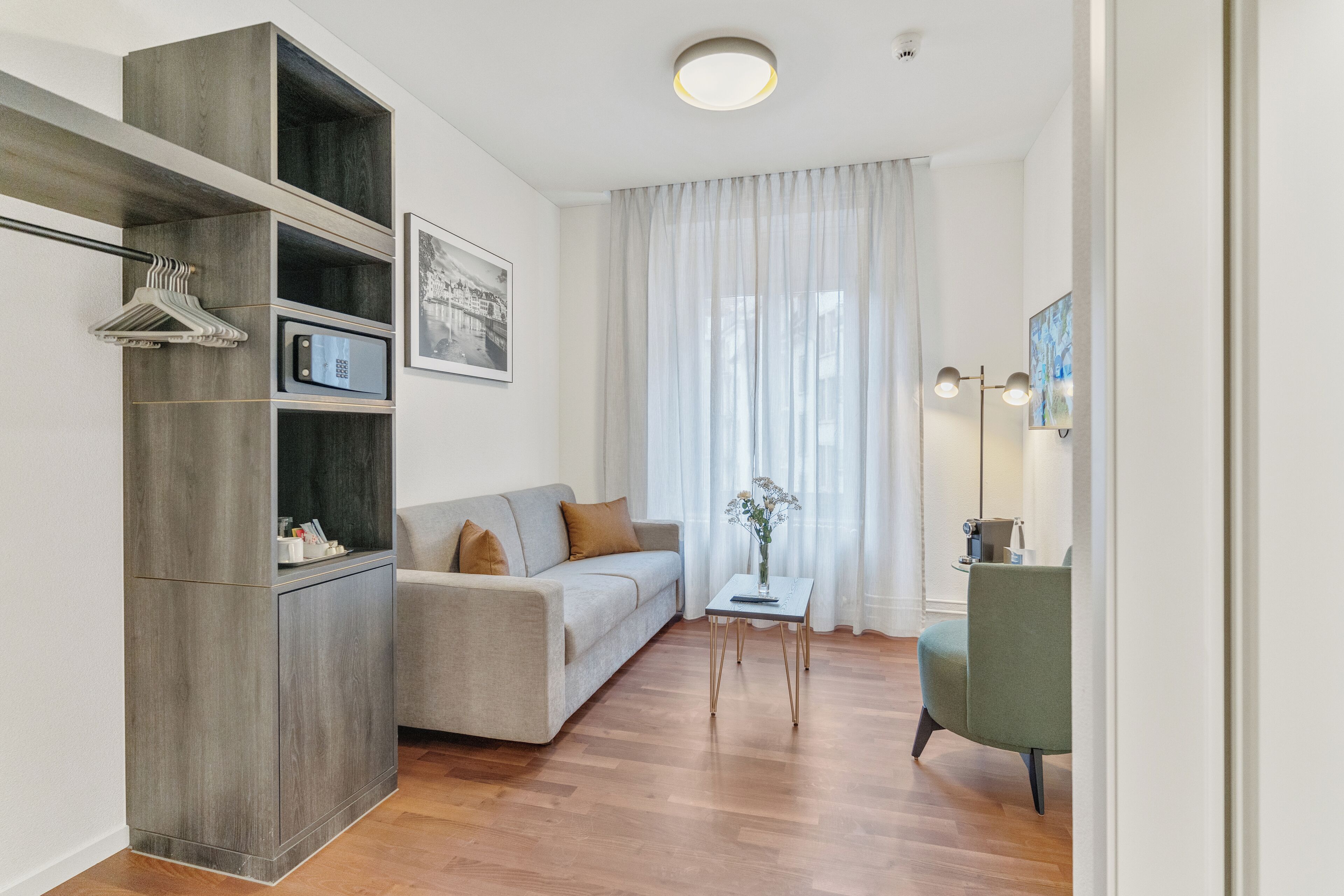 Una sala de estar moderna con un sofá gris, un mueble de madera, una mesita con un florero y un sillón verde.