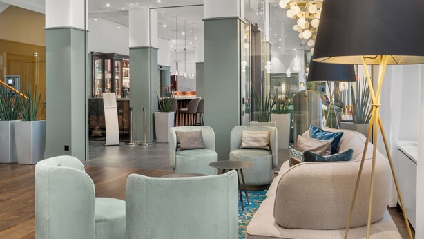Un hall d’entrée moderne, doté d’espaces aménagés avec des sièges, d’un grand lampadaire et offrant une vue sur la salle du restaurant.