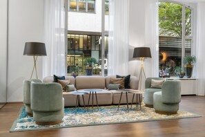 Relax in this inviting living space with a comfortable sofa, side tables, and floor lamps, surrounded by lush greenery and a scenic view.