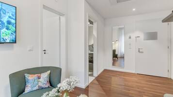 Une chambre d’hôtel moderne avec un plancher en bois, un fauteuil vert, un coussin coloré et un grand téléviseur à écran plat fixé au mur.
