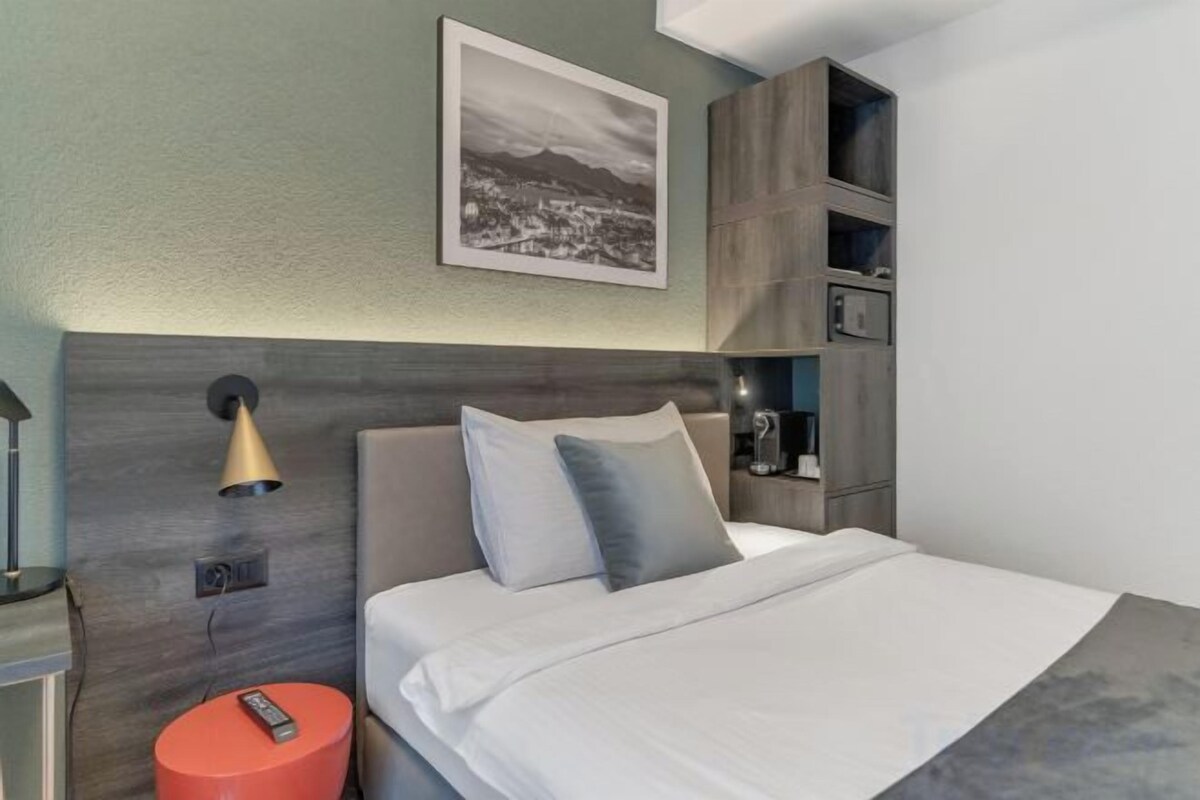 Une chambre d’hôtel moderne équipée d’un lit, d’une table de chevet, d’une lampe et d’une étagère sur laquelle est posée une photo.