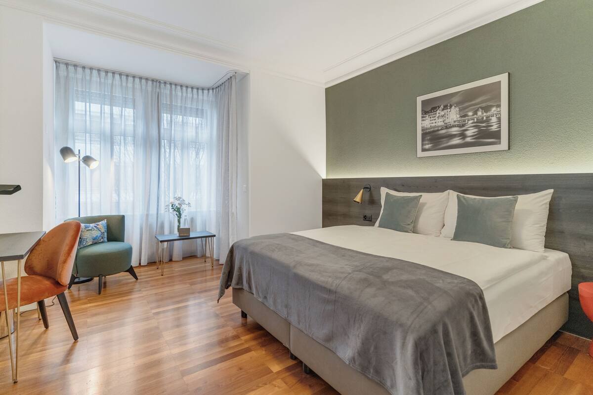 Une chambre d’hôtel avec un grand lit, un bureau, une chaise et une fenêtre avec des rideaux.