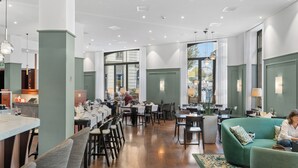 Un restaurant spacieux avec de hauts plafonds, de grandes fenêtres et un canapé vert dans l’espace réservé aux clients.