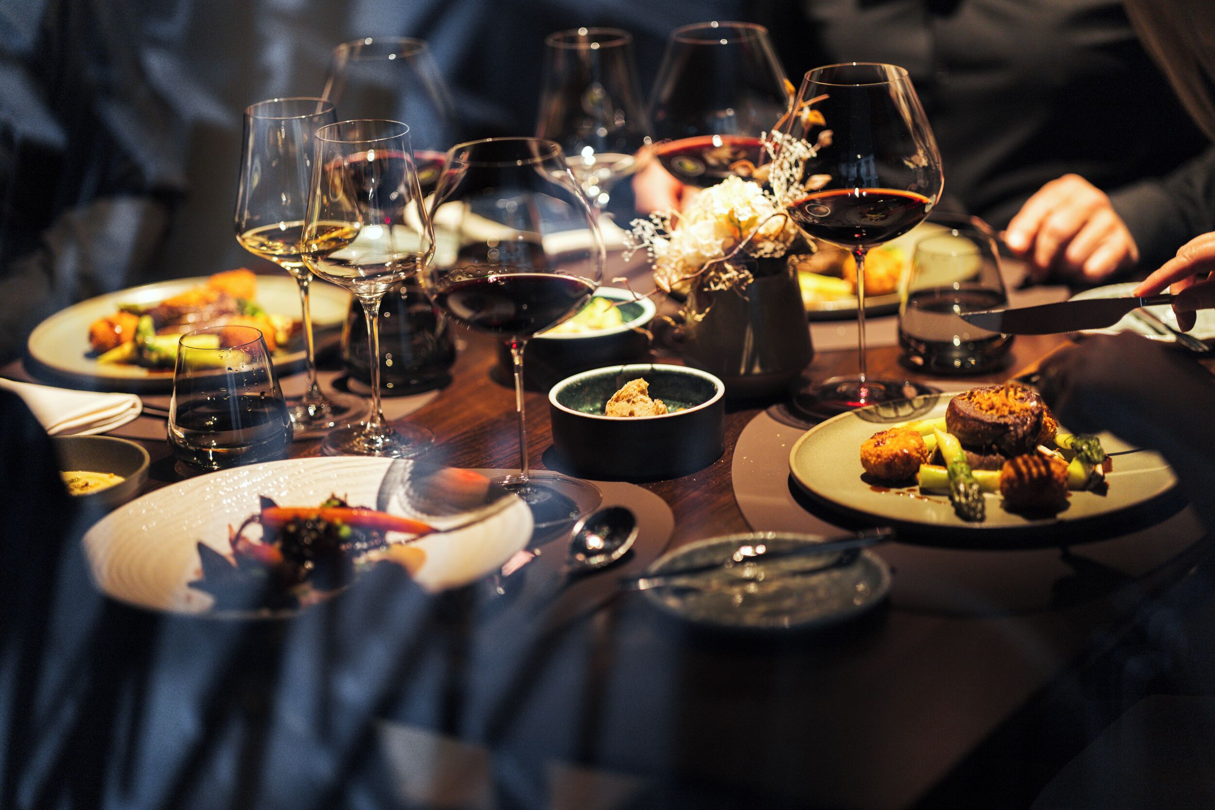 A dining table with multiple plates of food, wine glasses, and cutlery.