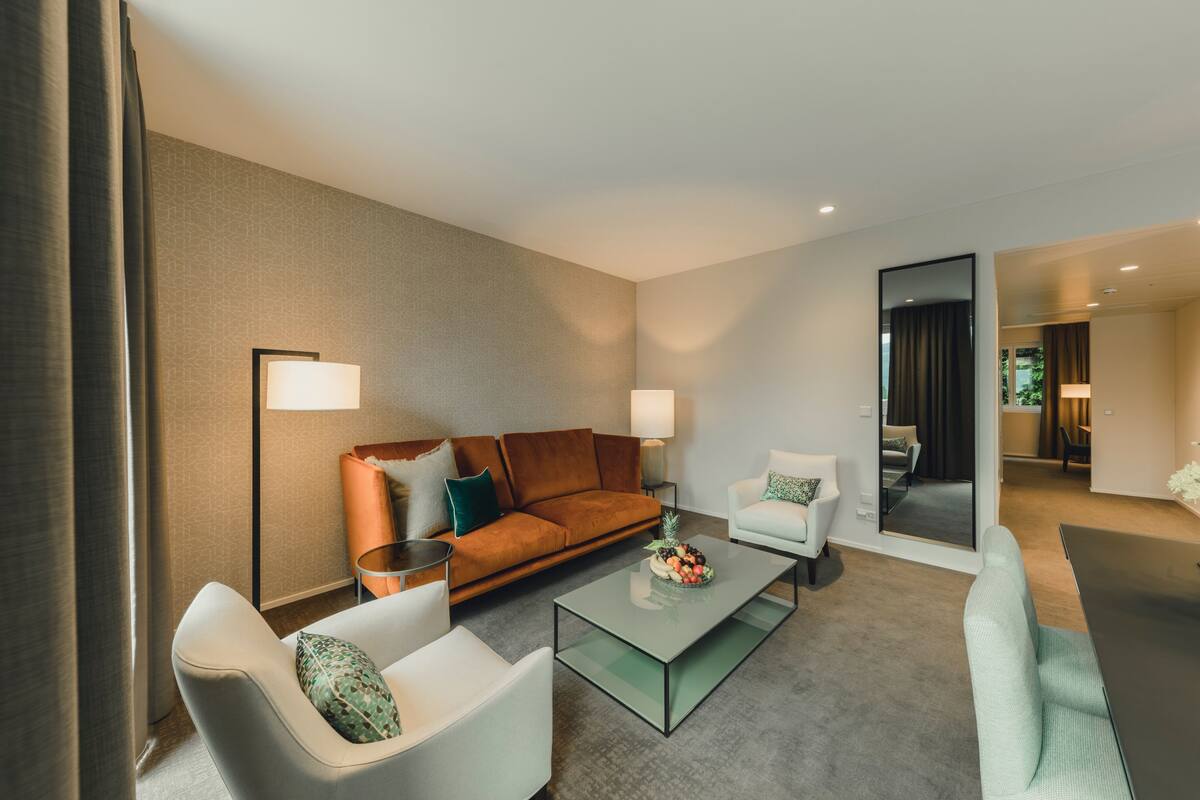 Una habitación de hotel moderna con sofá, sillones, una mesita de centro y una mesa de comedor.