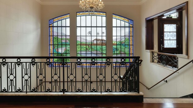 A staircase with a wrought iron railing, a chandelier, and stained glass windows with a landscape view. - Ibis Belo Horizonte Liberdade (Belo Horizonte)