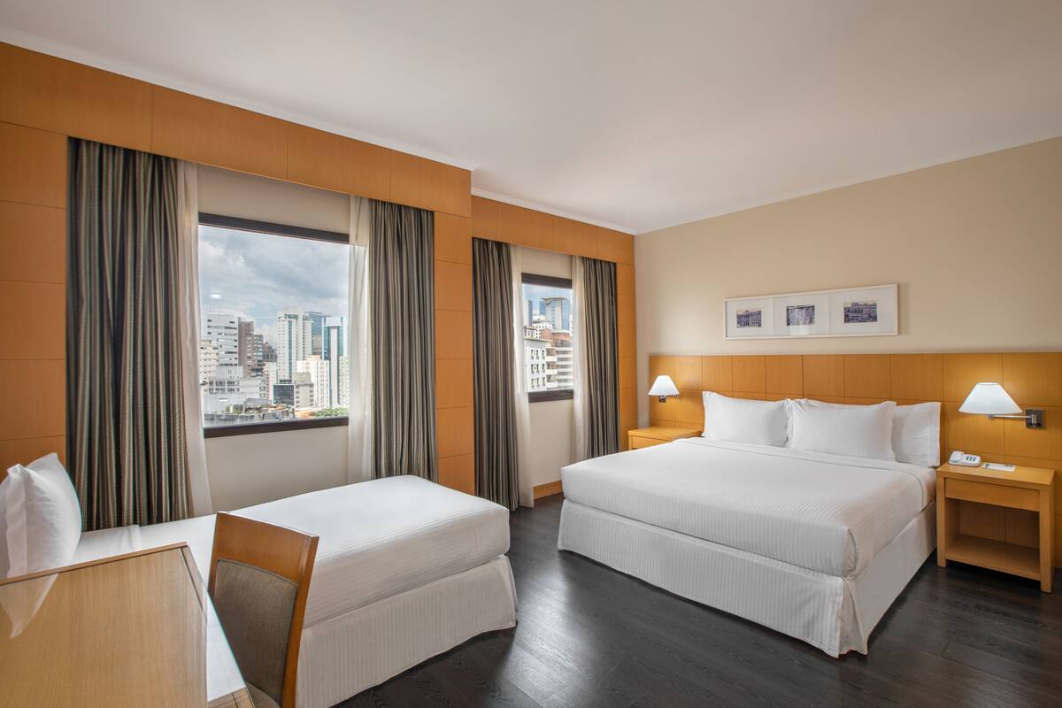 Ein Hotelzimmer mit zwei Betten, einem Schreibtisch und Blick auf die Stadtlandschaft.