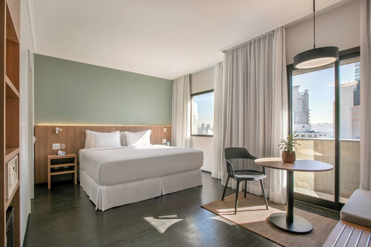 Ein Hotelzimmer mit Bett, Nachttisch, Stuhl und einem kleinen Tisch mit Pflanze.