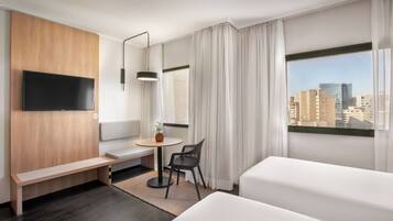 A hotel room with a bed, a desk, a chair, a TV, and a window with a city view.