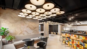 Un área de bar moderna con pared de diseño geométrico, diversas opciones de asientos e iluminación circular en el techo.