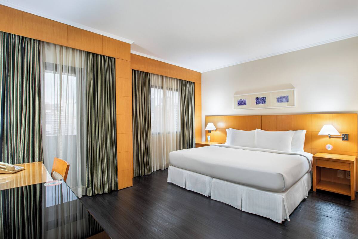 Ein Hotelzimmer mit einem großen Bett, zwei Nachttischen inklusive Lampen, einem Schreibtisch mit Telefon und einem Sessel.