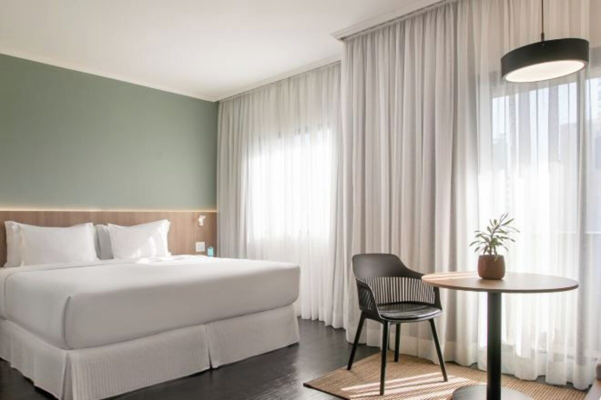 Una habitación de hotel con una cama grande, una silla, una mesita y una planta en maceta.