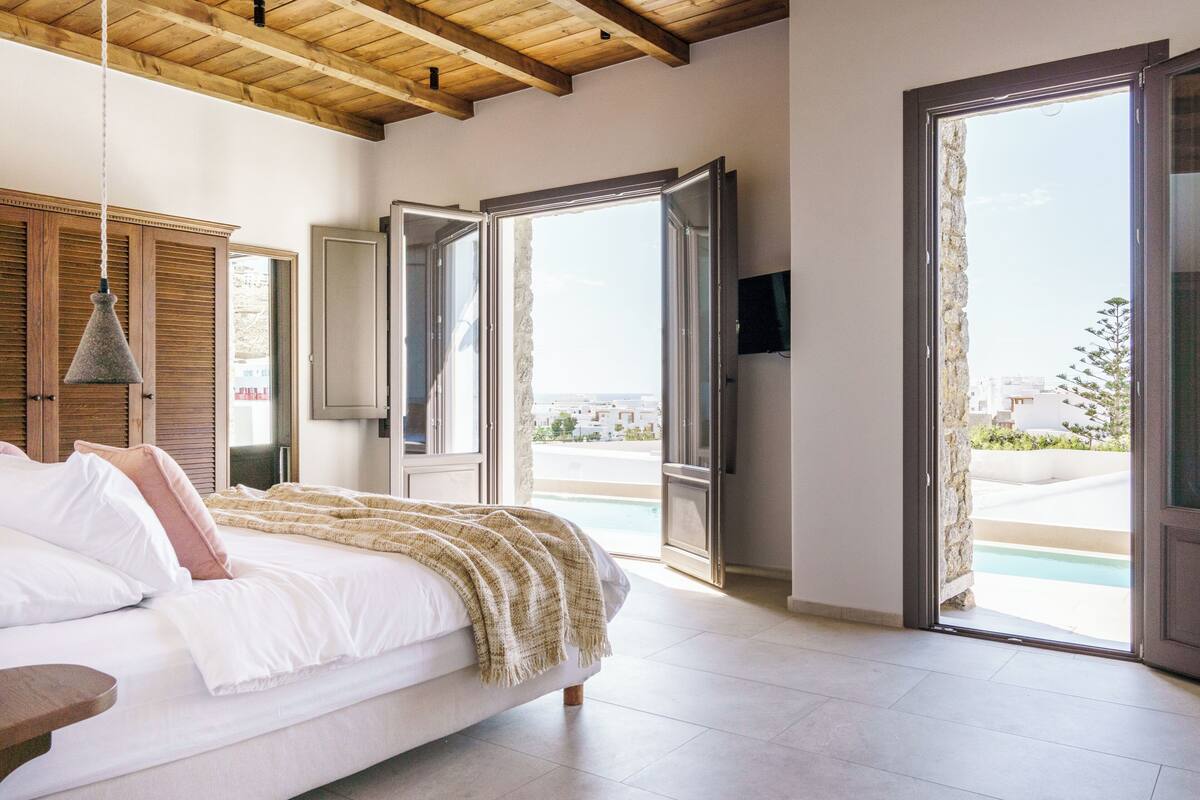 Un dormitorio con cama, techo de madera, televisor y vista a una piscina.
