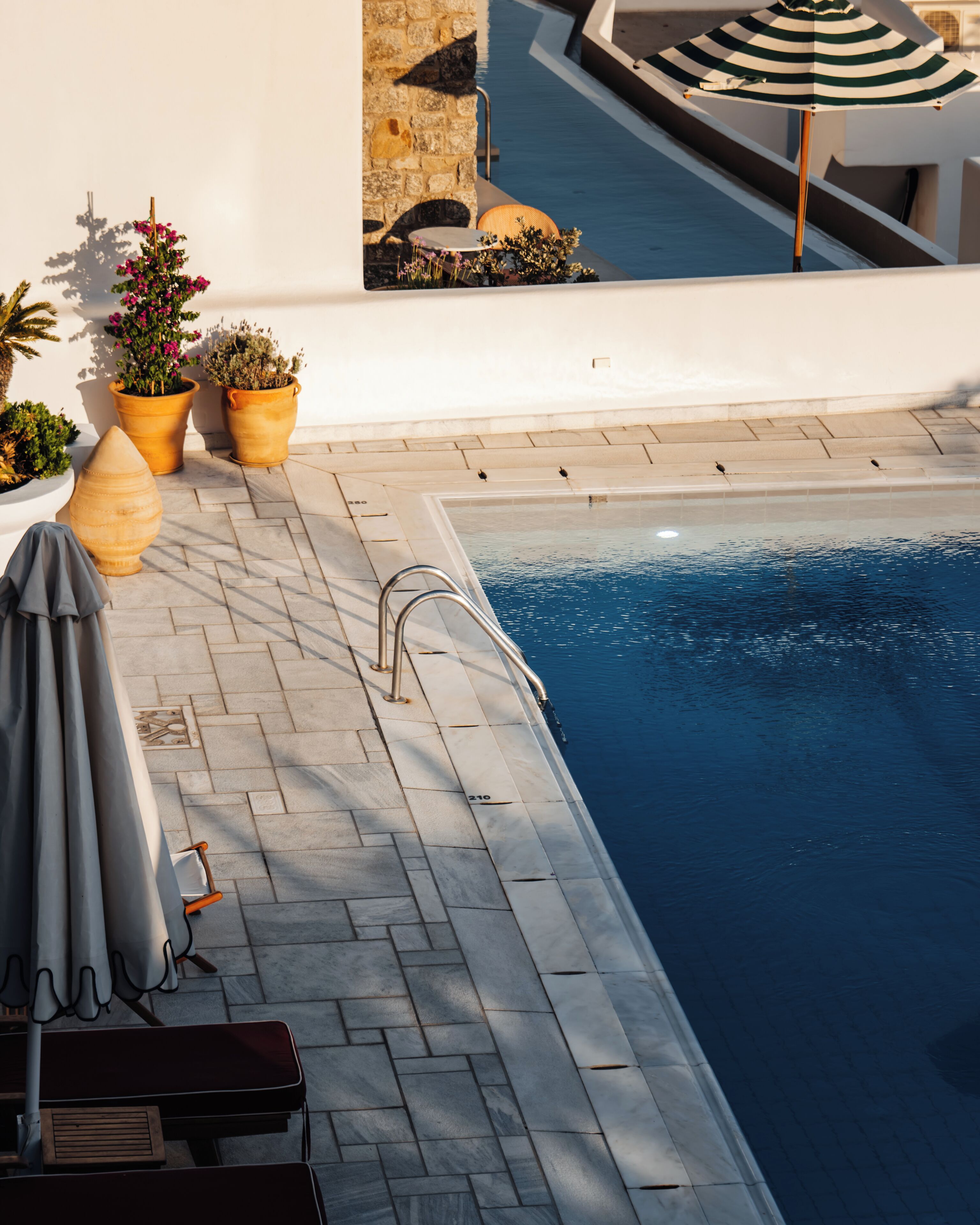 A poolside area with a stone wall, potted plants, and a lounge chair.