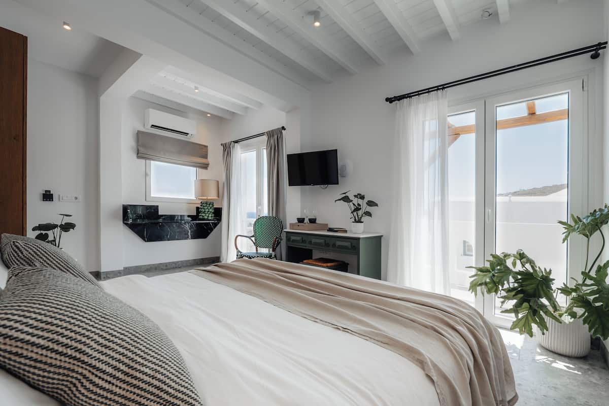 Un dormitorio moderno con cama, escritorio, silla, televisión y ventanas amplias.