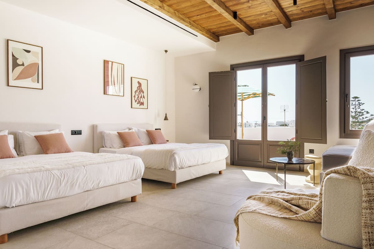 Una habitación de hotel moderna con dos camas, una mesita y vistas al exterior.