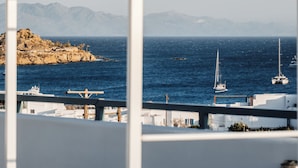Uma varanda com vista para o mar, barcos e um litoral rochoso.