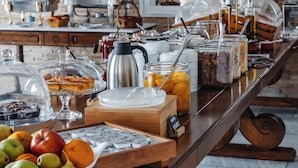 Um buffet de café da manhã com diversos alimentos e bebidas, uma cafeteira e um relógio na parede.