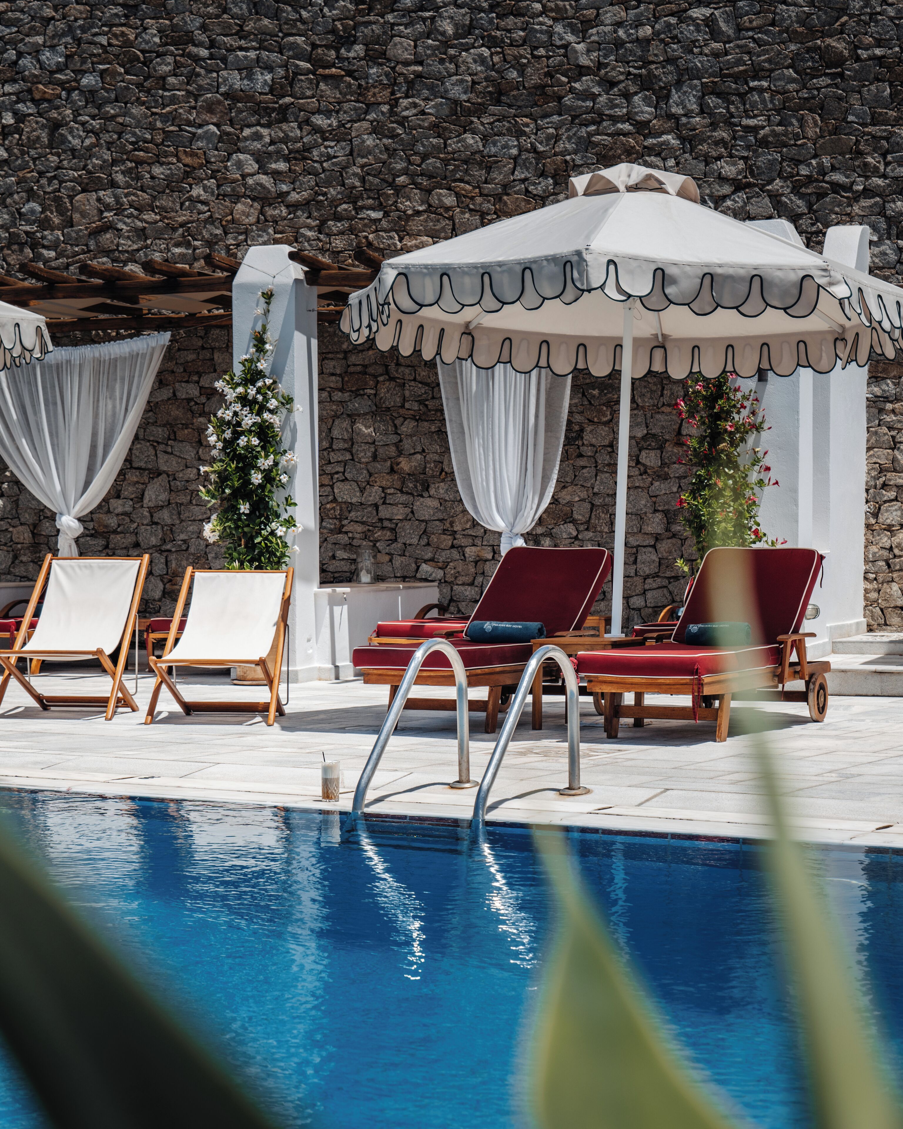 A poolside area with lounge chairs and a stone wall backdrop.