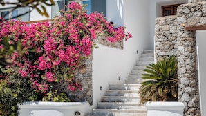 Um edifício branco com parede de pedra, escadaria de madeira e flores cor-de-rosa.