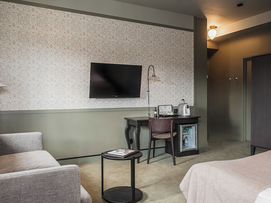 Une chambre d’hôtel équipée d’une télévision à écran plat, d’un bureau avec un ordinateur portable, d’un petit réfrigérateur et d’un lit.