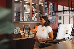 A bar area with a computer, a cash register, and a shelf with various bottles and snacks.