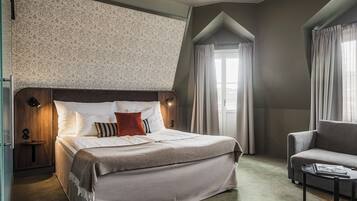 A hotel room with a large bed, a sofa, a small table, and a window with curtains.
