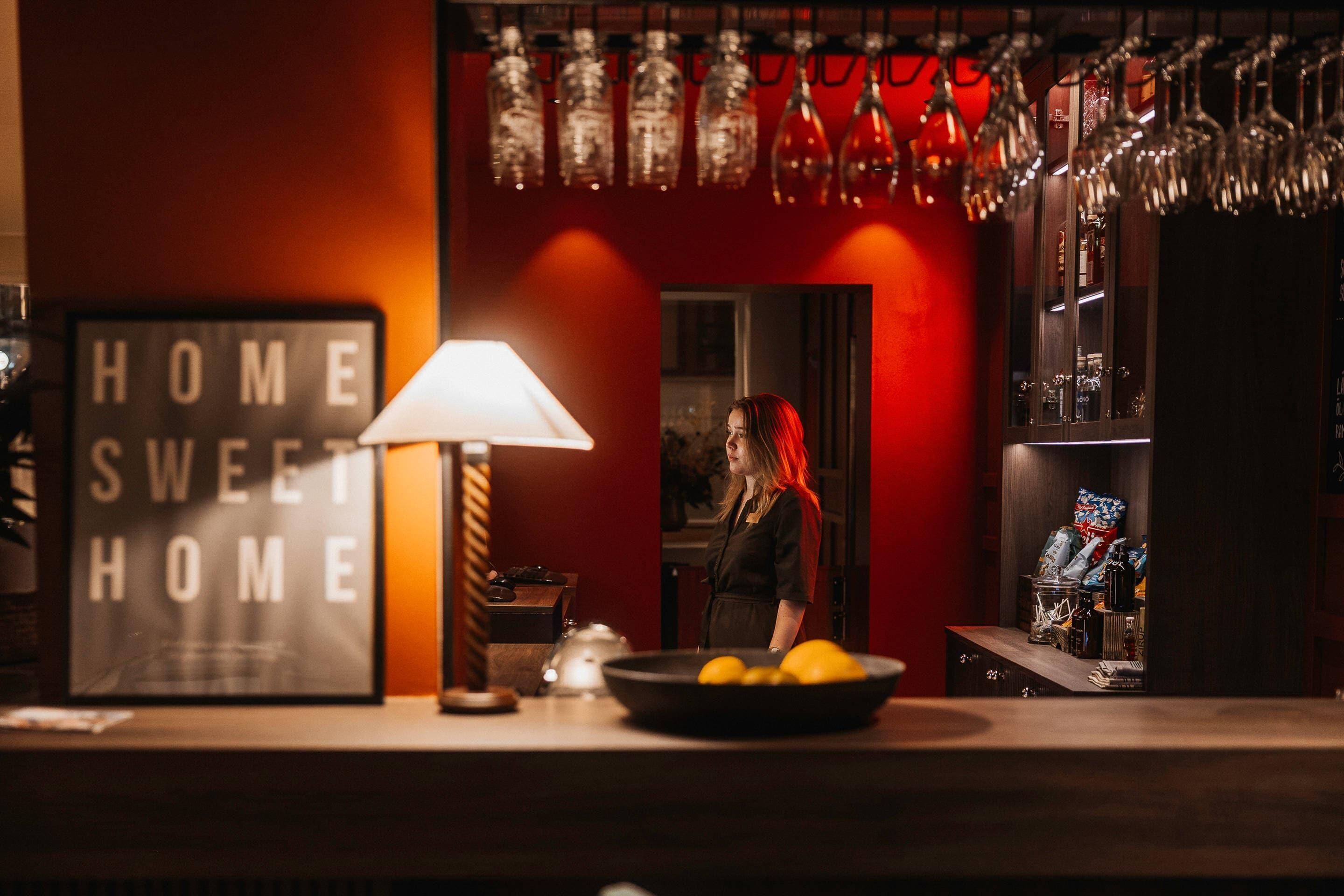 A bar area with a sign reading "HOME SWEET HOME," a bowl of lemons, and a woman standing in the background.