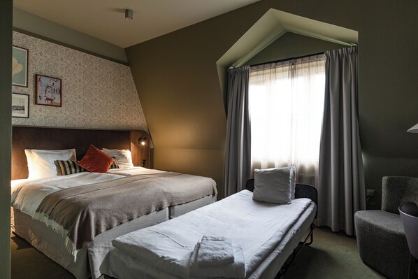 A hotel room with two beds, a chair, a window with curtains, and wall art.