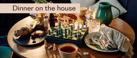 A cozy dining setup with a chessboard, a cup of tea, and a plate of food on a round table.