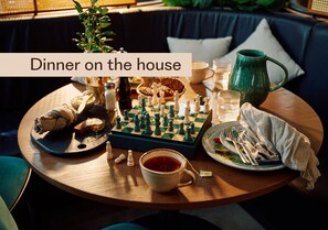 A cozy dining setup with a chessboard, a cup of tea, and a plate of food on a round table.