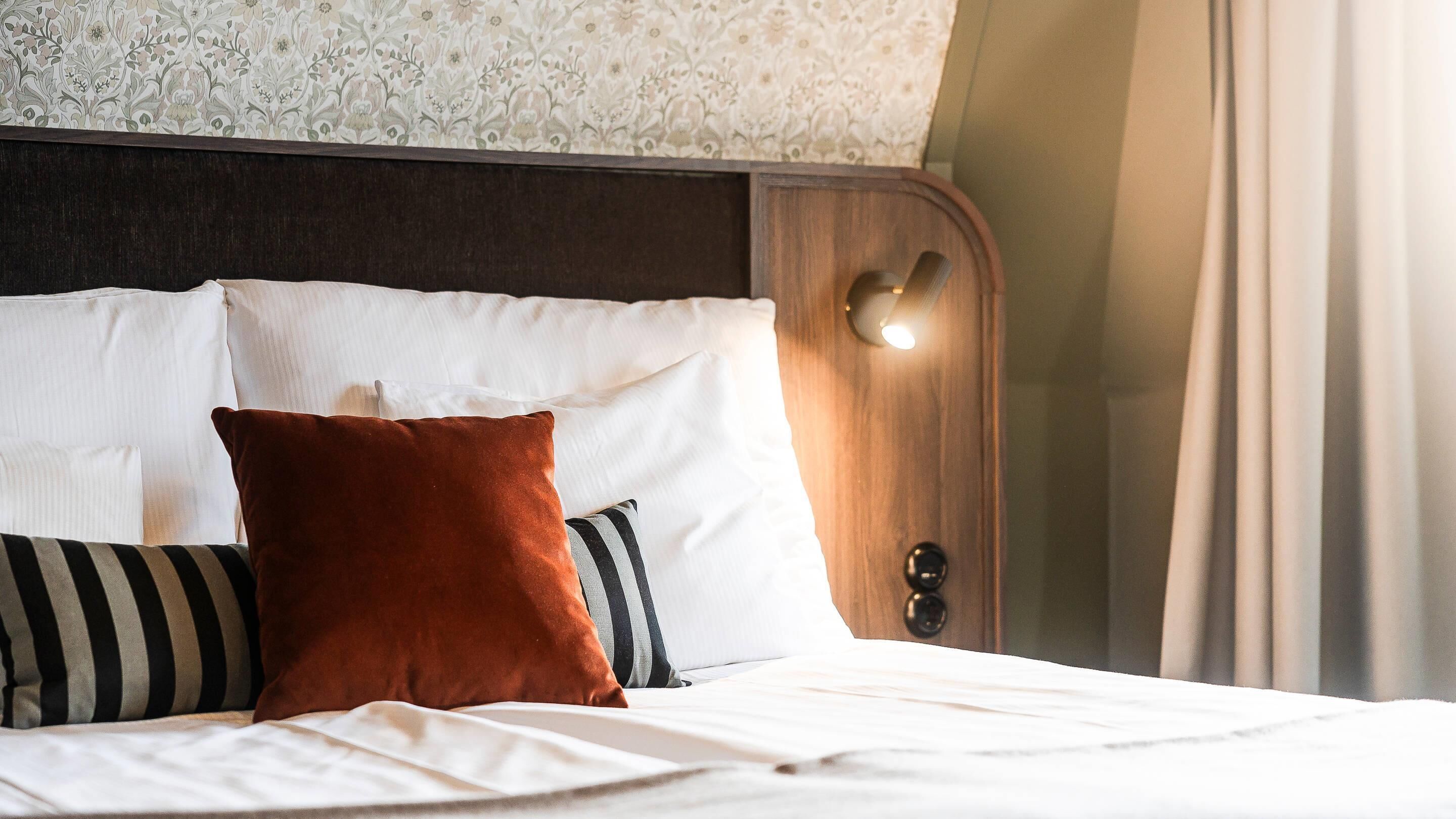A neatly made bed with white linens and a variety of pillows, including a striped one and a brown one.