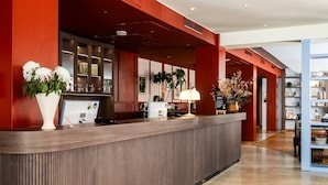A reception desk with a wooden finish, a white vase with flowers, a digital screen, and a signboard. - Home Hotel Grand Sundsvall (Sundsvall)