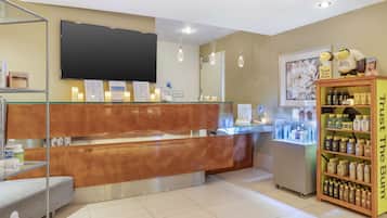 Un área de recepción con mostrador de madera, un televisor montado en la pared, una estantería con productos y una vitrina con artículos.