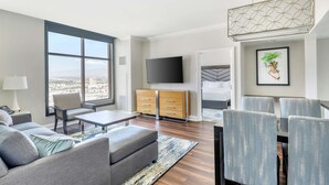 Un salon moderne doté d’une grande fenêtre, d’un téléviseur à écran plat, d’un meuble en bois et d’un coin repas avec des chaises.