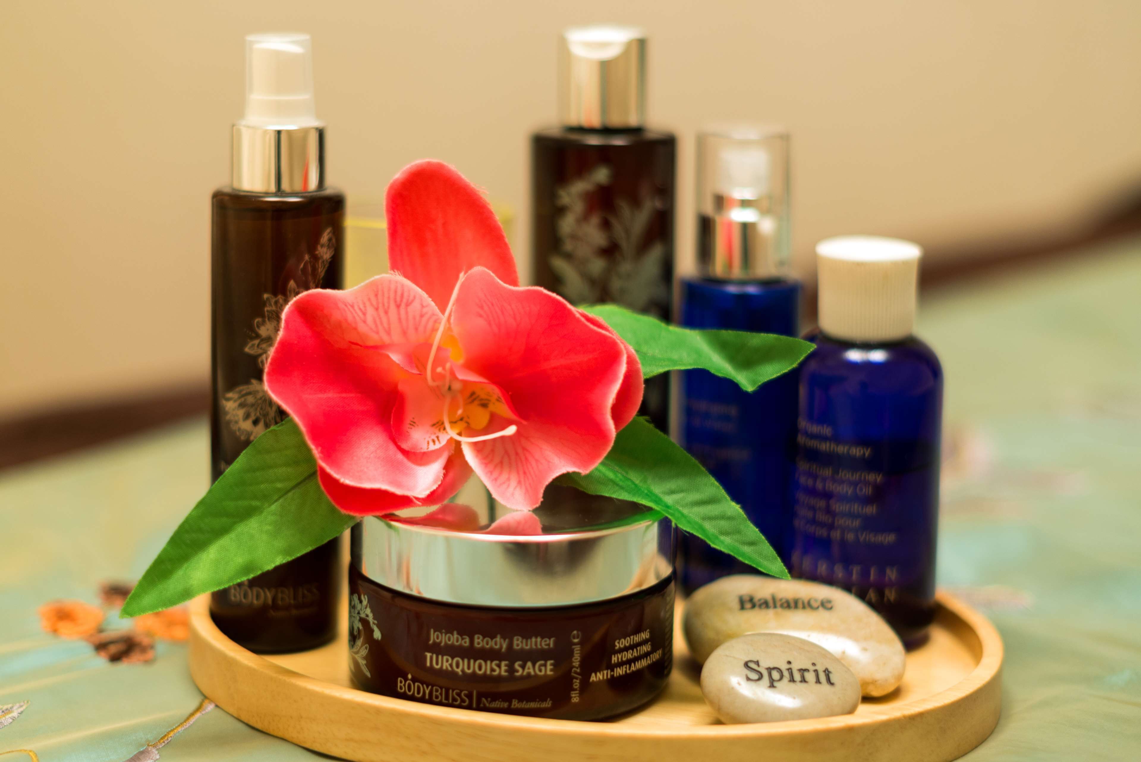 A wooden tray with a jar of body butter, a red orchid, and several bottles of essential oils.