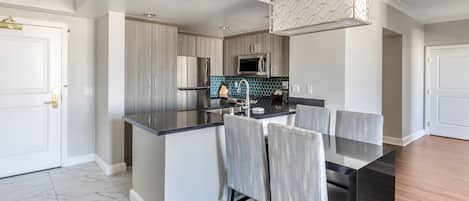 Cocina moderna con una isla central, sillas tapizadas en gris y una lámpara colgante.