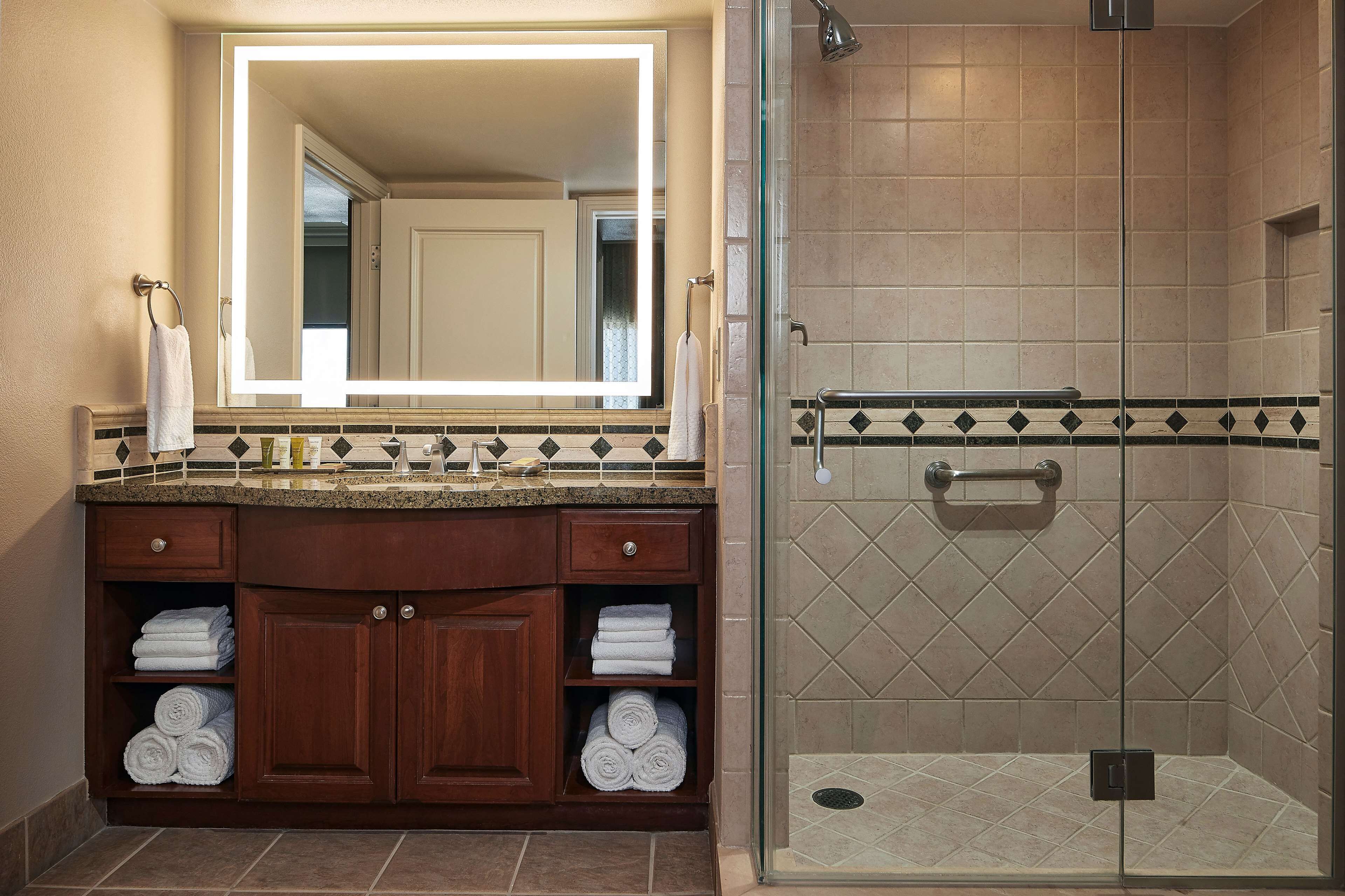 A bathroom with a large mirror, wooden vanity, and a glass-enclosed shower.