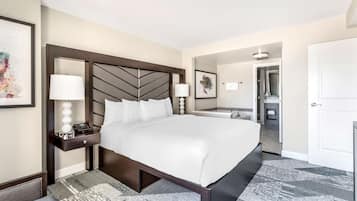 A hotel room with a large bed, a bedside table with a lamp, a nightstand, and a framed picture on the wall.