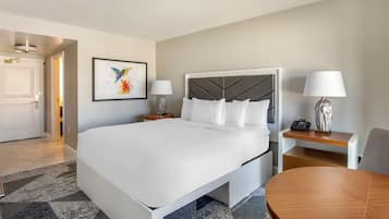 Une chambre d’hôtel moderne avec un grand lit, une table de chevet avec une lampe, une petite table avec une lampe et une œuvre d’art encadrée accrochée au mur.