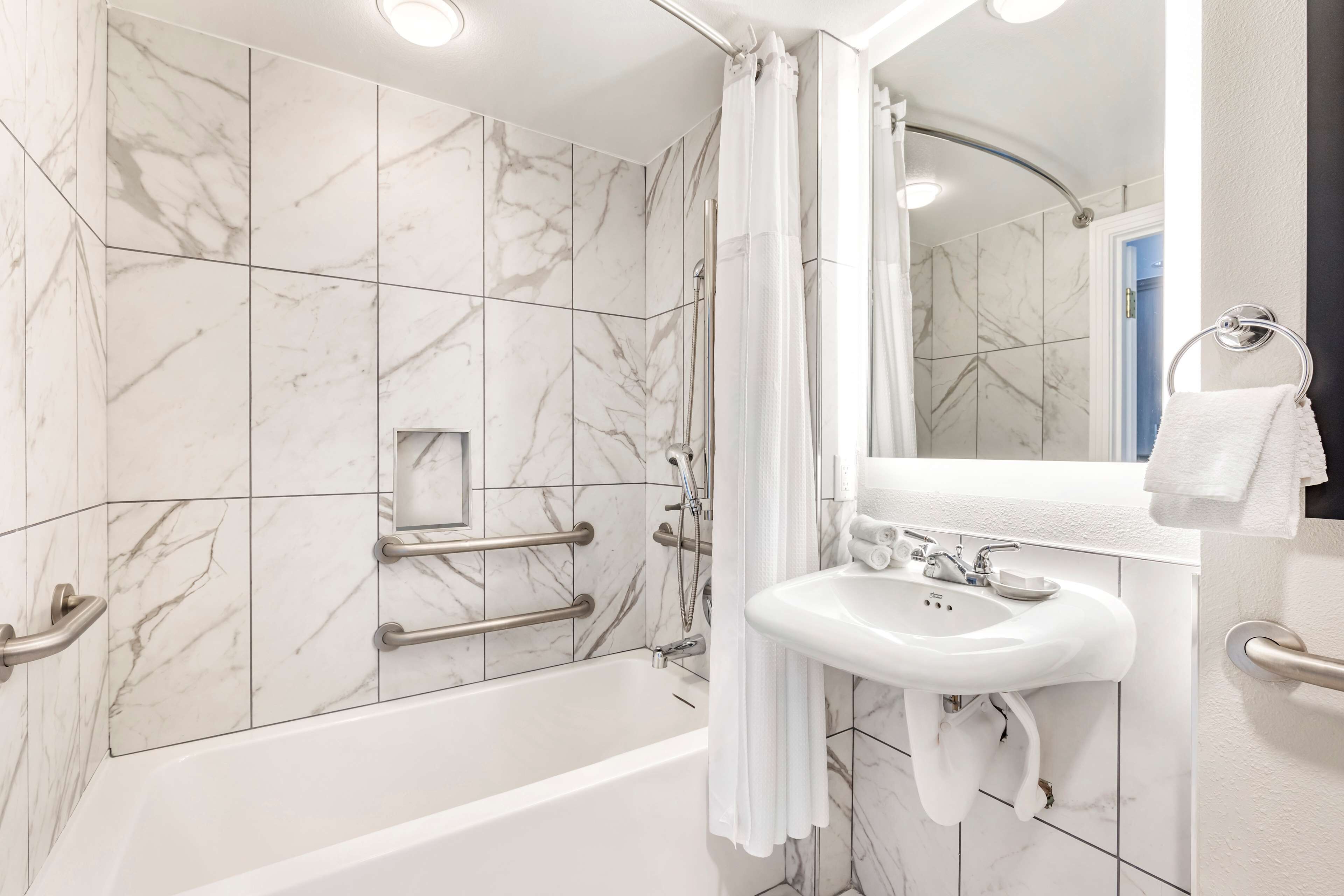 A modern bathroom with a bathtub, shower, and sink, featuring marble tiles and handrails.