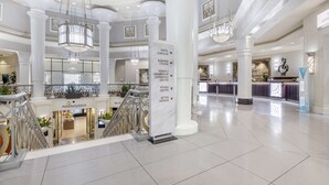 A spacious hotel lobby with a central column displaying directional signs, a fitness center, and a membership experience area.