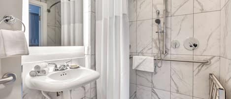 Une salle de bain moderne avec un lavabo blanc, des carreaux de marbre, une douche avec une porte en verre et un porte-serviettes apparent.