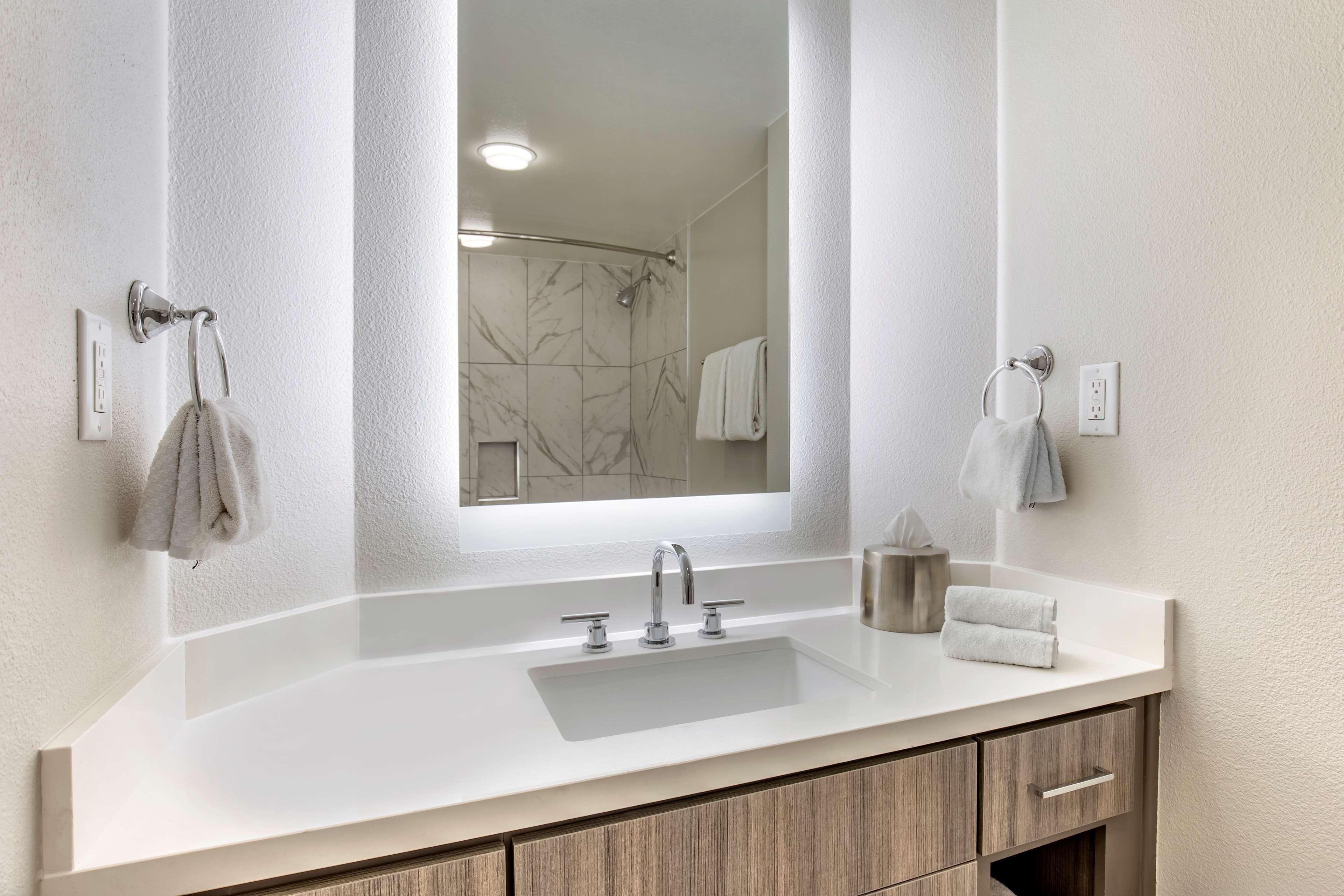 A modern bathroom with a large mirror, a white sink, and wooden cabinets.