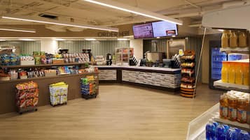 A grocery store interior with a checkout counter, shelves stocked with various products, and a refrigerated display.